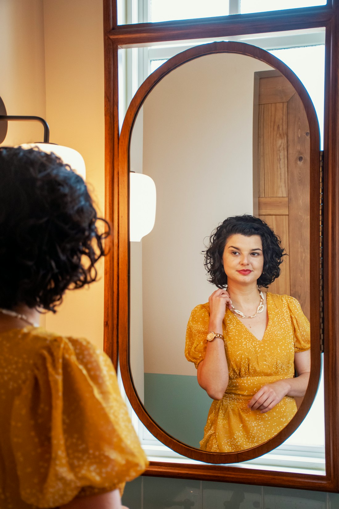 A woman in an orange dress checking the fit in a mirror